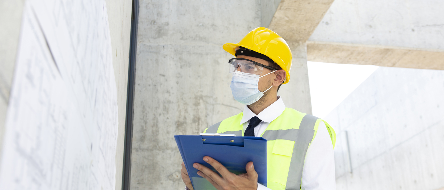A worker in safety gear holds a checklist while inspecting a building.