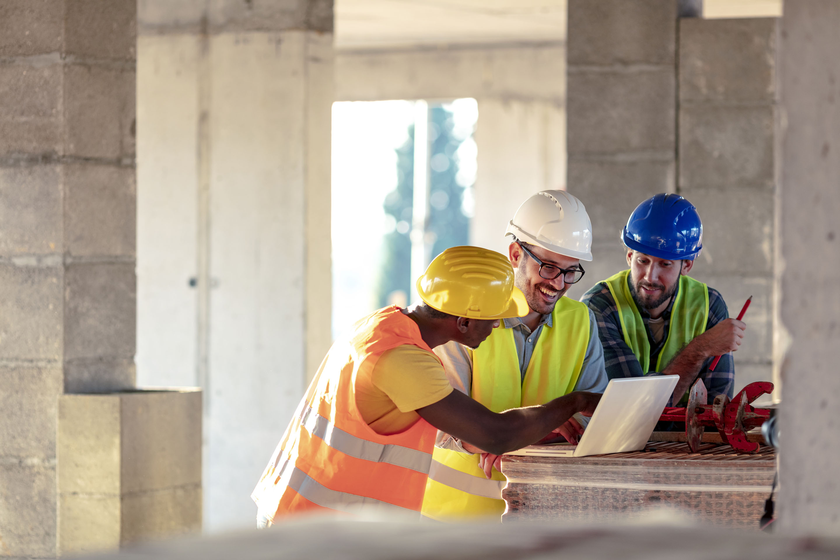 Team of Multi-Ethnic construction workers wearing protective helmets and vests discussing project details with executive supervisor standing with tools and laptop.