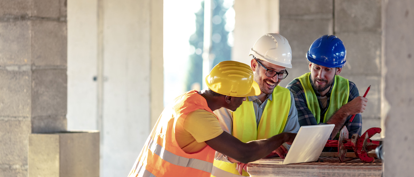 Three contractors discuss construction insurance while standing in an unfinished building.