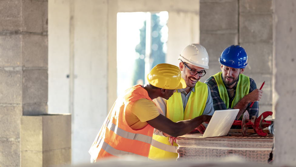 Three contractors conferring over laptop in an unfinished building.