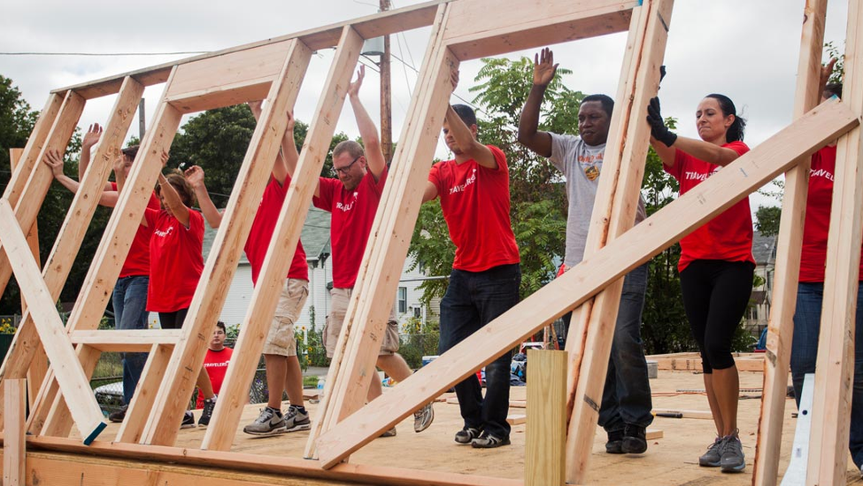 Volunteers lift wooden wall framing into position.