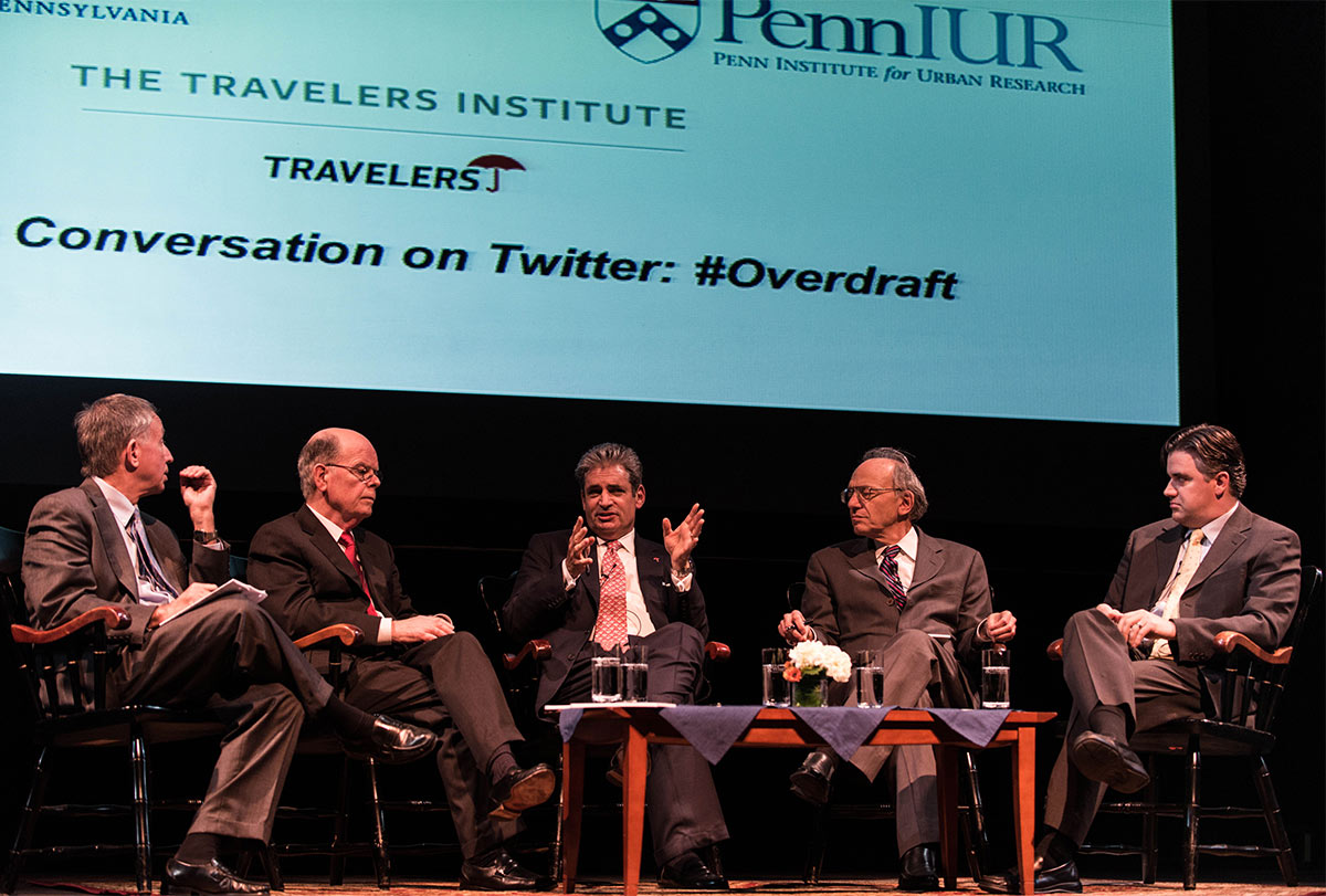 Five panelists seated on stage below presentation projection that reads The Travelers Institute, Travelers, Conversation on Twitter: #Overdraft