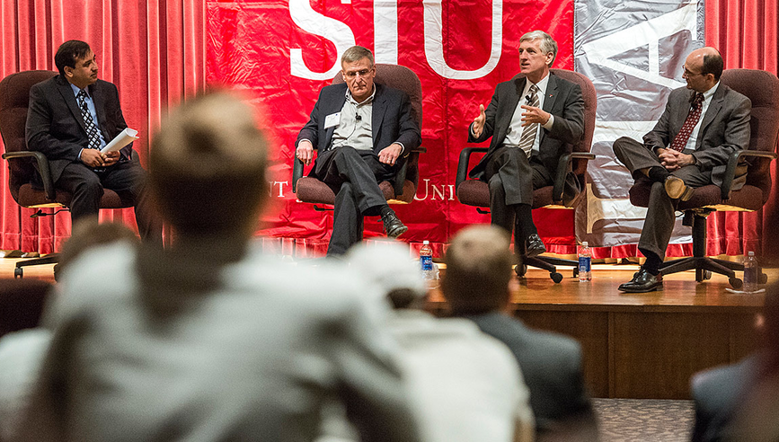 A panel of four men speaking on stage