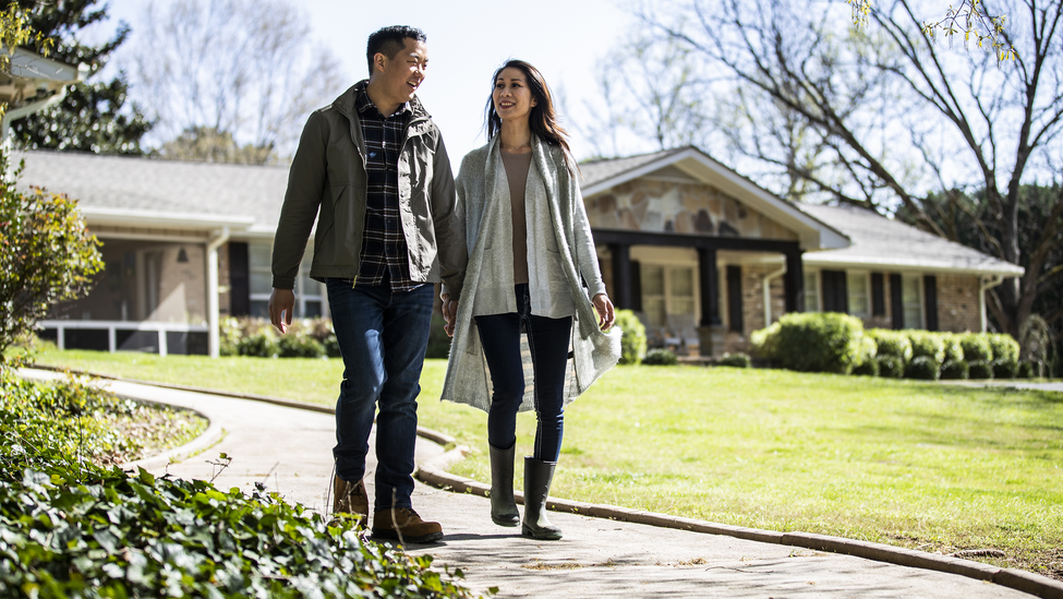 Couple walking outside in front of a house.