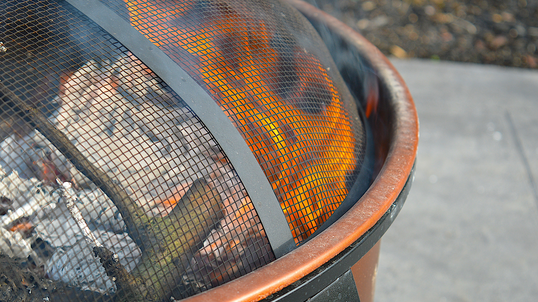 A fire pit in a backyard, covered by a mesh wire screen.