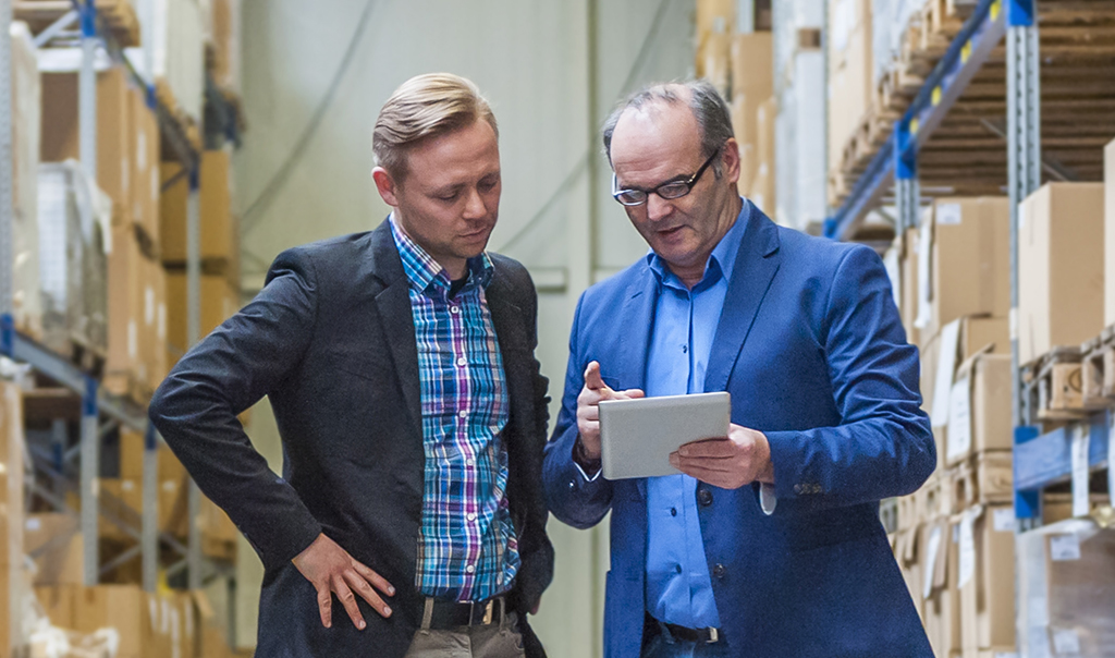 Two business professionals having a meeting in a warehouse and looking at smart device