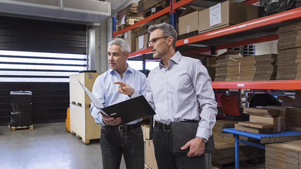 Two male professionals having a meeting in a warehouse and looking at products