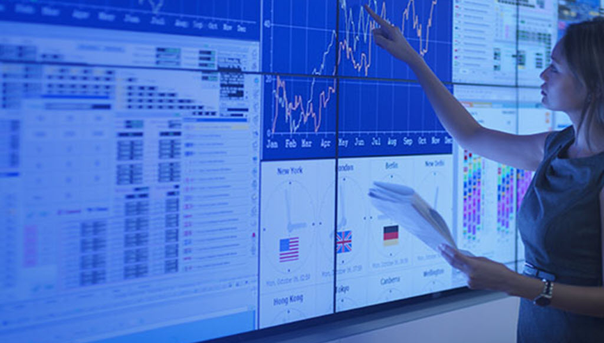 A person pointing at a line graph on a large screen.