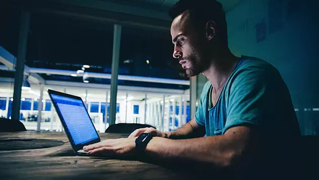 Cyber criminal looking at company information on laptop