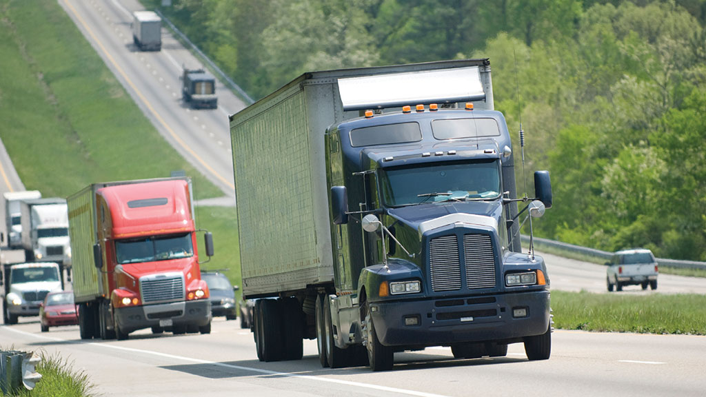 Alt Text   dark blue large commercial truck driving along an interstate highway