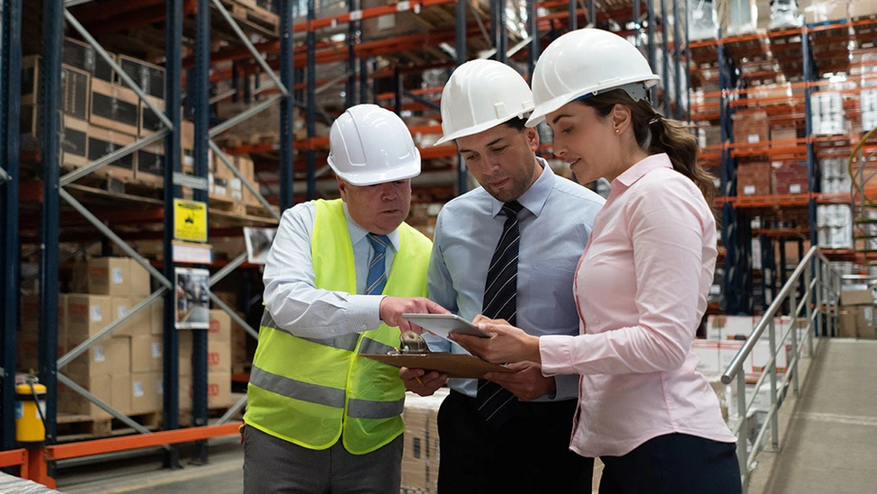 Warehouse employees wearing hardhats holding clipboard