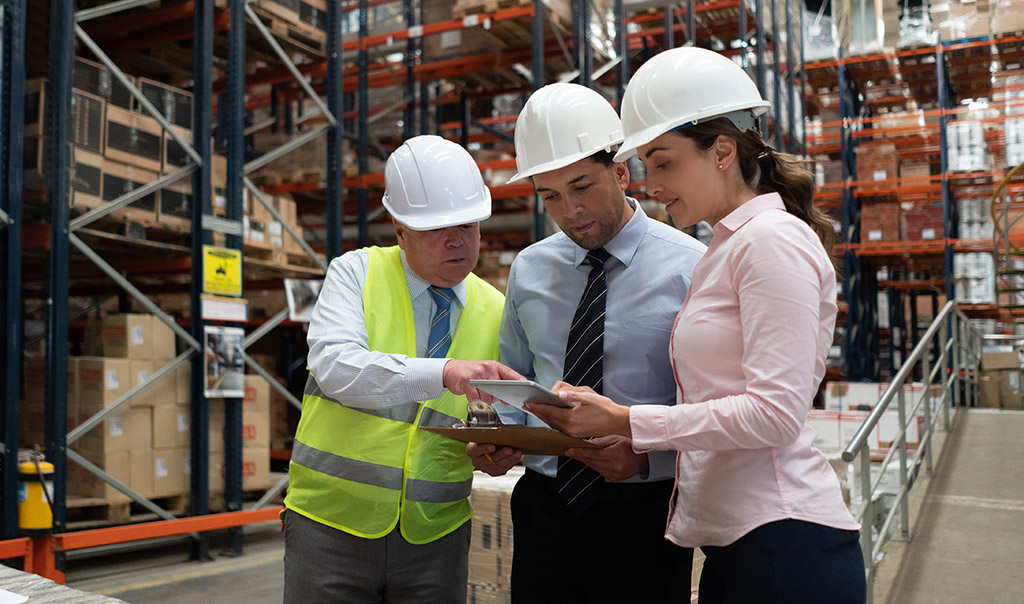 Warehouse employees, wearing a hardhat, holding clipboard and digital tablet