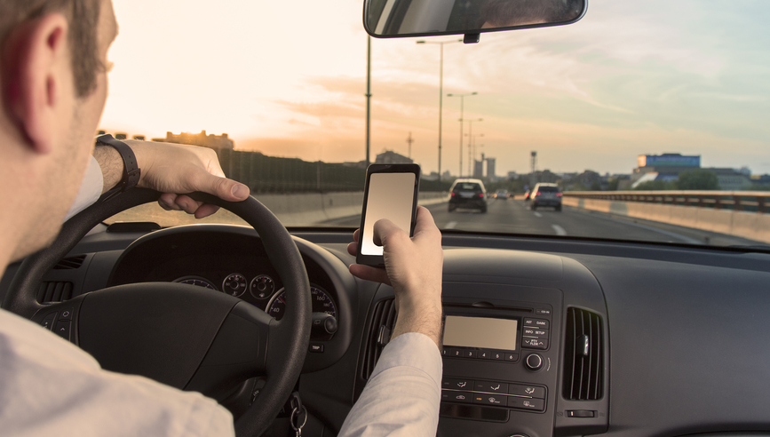 A man texts on his cellphone while driving a car.