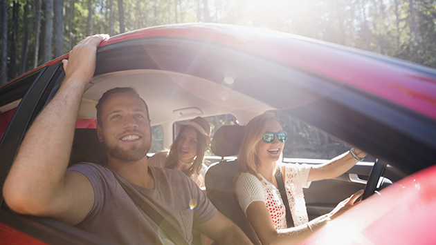 Friends riding safely in a car with the windows down during the summer.