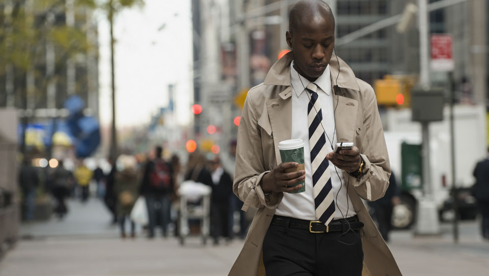 Man walking on a busy sidewalk and distracted looking at phone and listening to music.