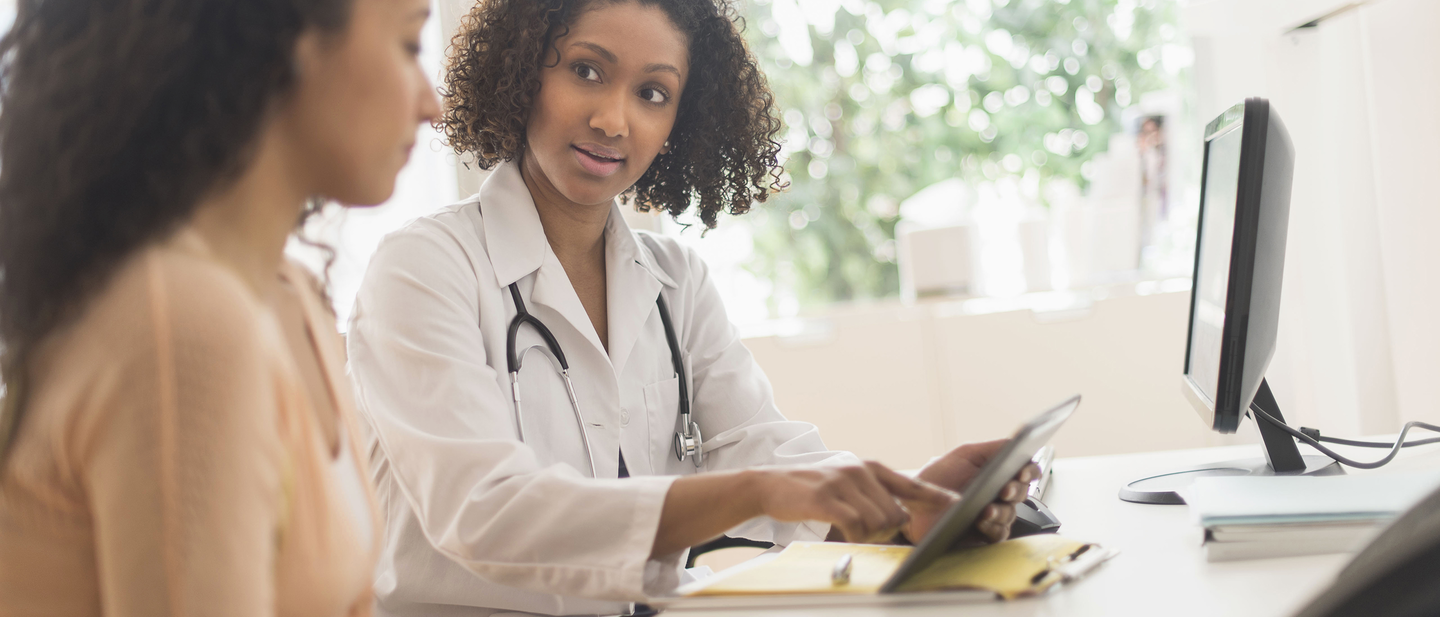 A doctor in a lab coat with a stethoscope discussing something with a patient.