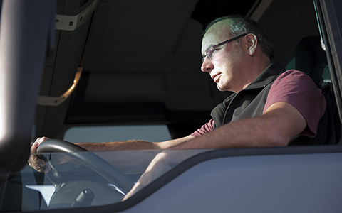 Driver sitting in truck stares ahead with one hand on steering wheel