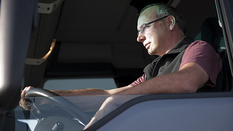 Driver sitting in truck stares ahead with one hand on steering wheel