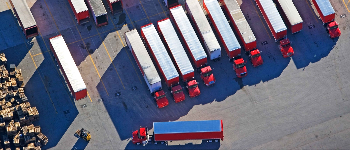 Drone view of a fleet of red and white freight trucks in a large lot.