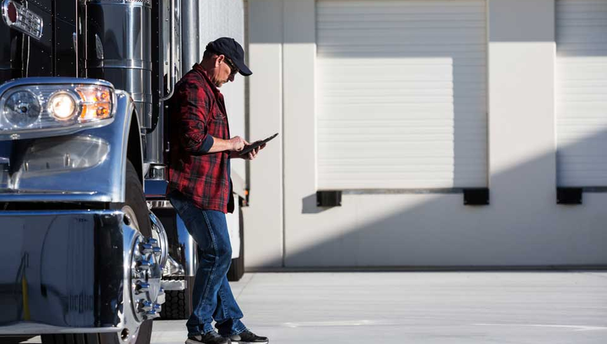 Truck driving looking at tablet and leaning against tractor truck