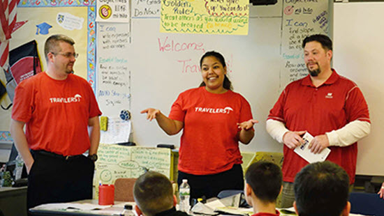 three Travelers volunteers talking at the front of a classroom