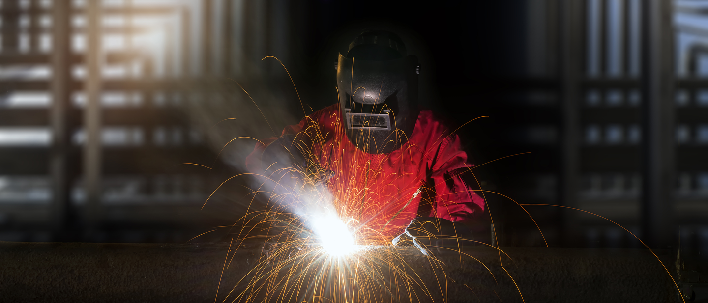 Welder in safety gear welding in dark room, sparks flying dramatically.