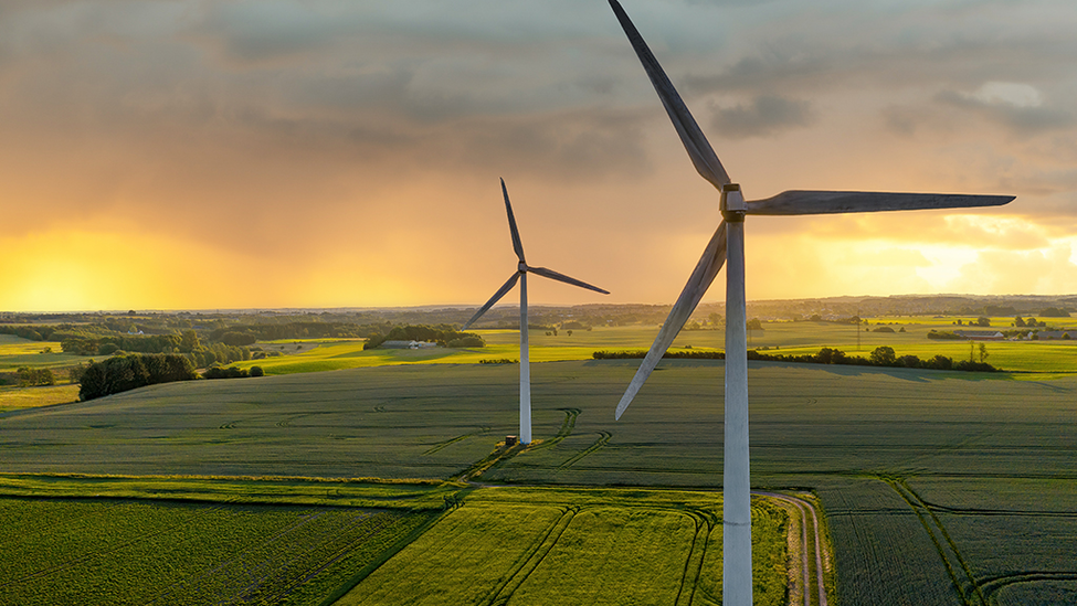 Two wind turbines in an open landscape with mountains in the far distance.