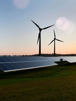 Landscape view of solar farm at sunset, with wind turbines in the background.