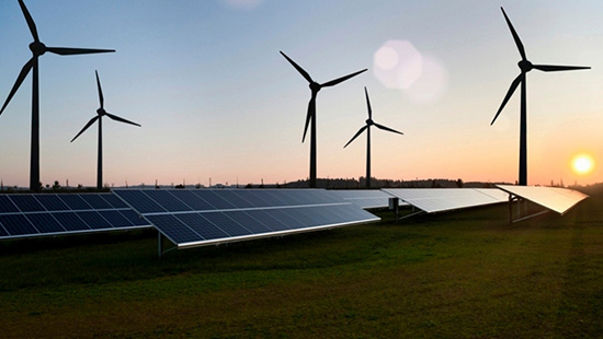 Landscape view of solar farm at sunset, with wind turbines in the background.