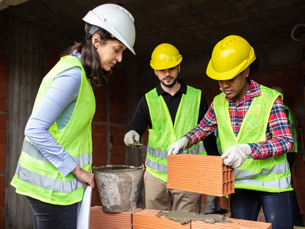 Three construction workers build a structure with bricks and mortar.