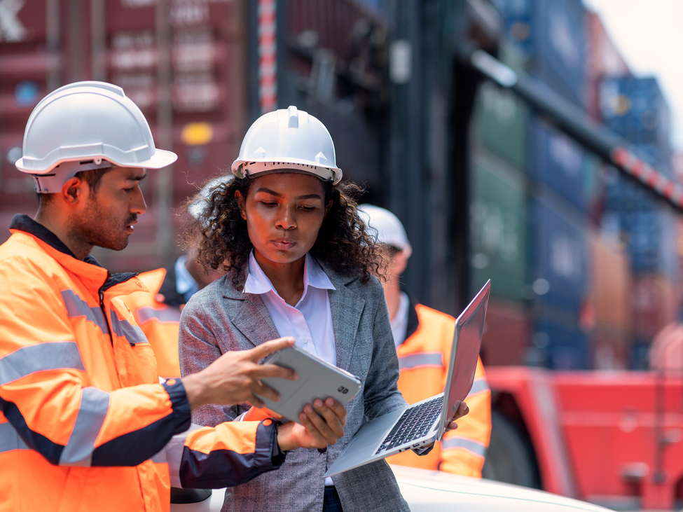 A safety inspector and logistics manager compare notes and discuss risks at a shipping yard.