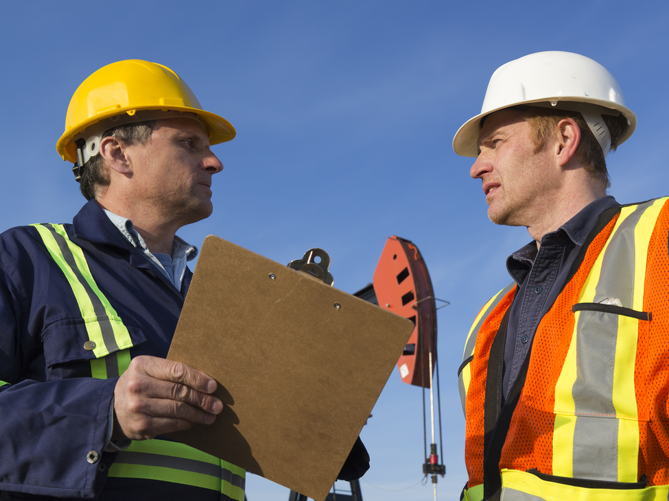 Two energy executives discuss oil well control services outdoors near field equipment.