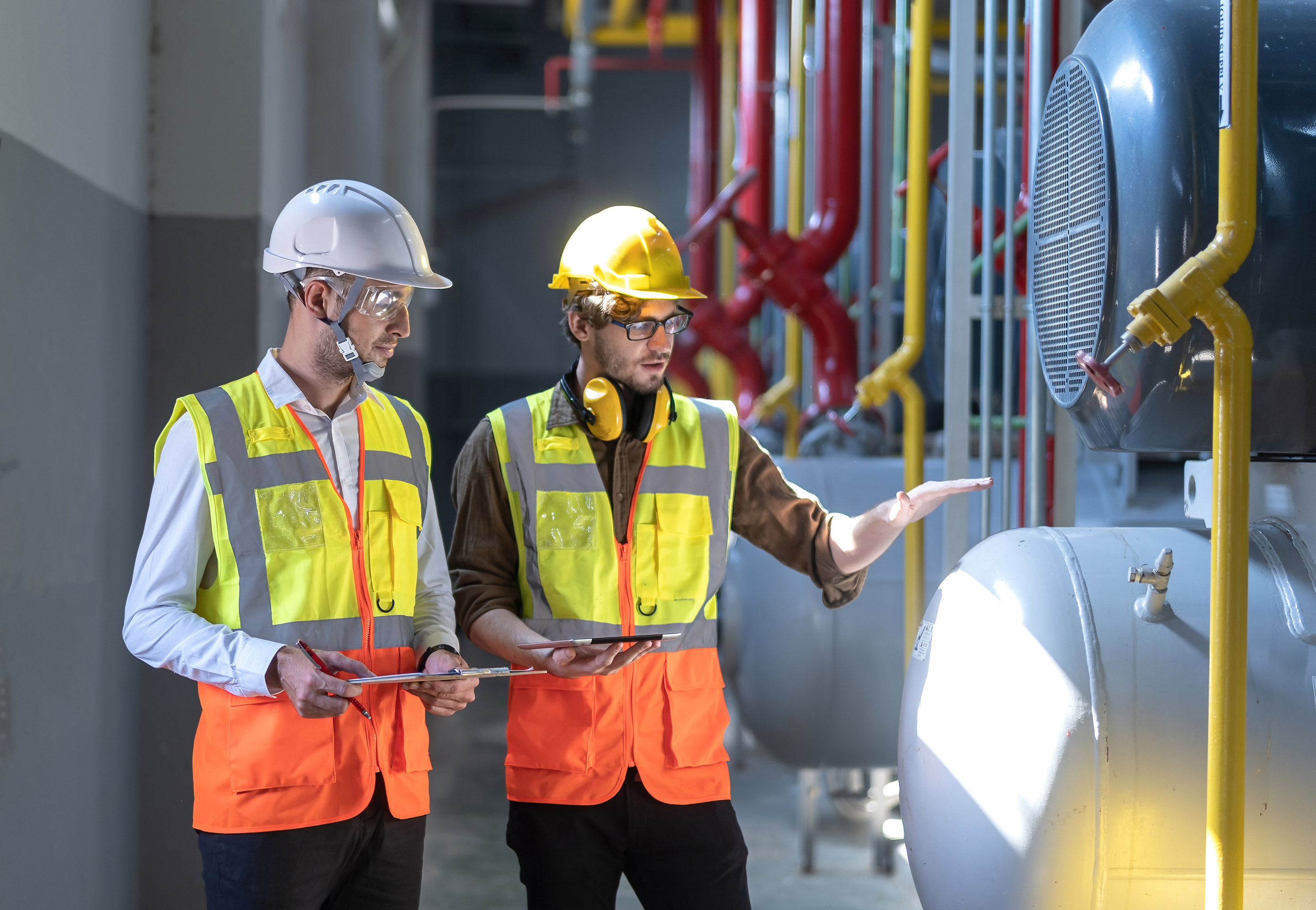 Two engineers working at an oil and gas factory, looking at a pipeline and pump.