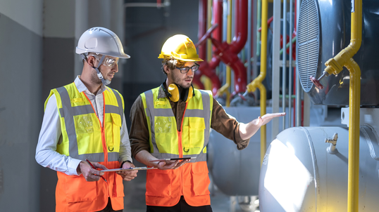 Two engineers working at an oil and gas factory, looking at a pipeline and pump.