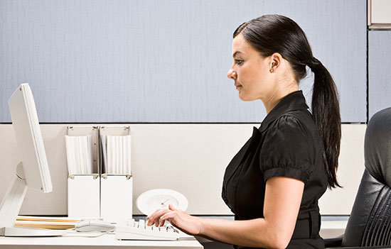 A woman sitting at a desk in an office, typing on a keyboard.