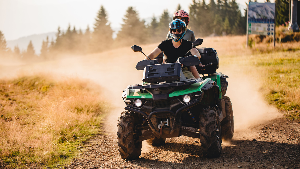 People riding an ATV vehicle on a dirt road.