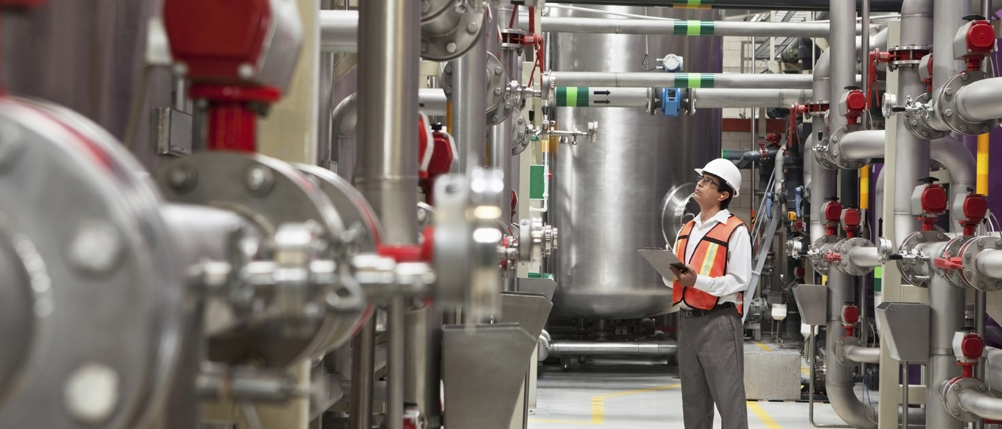 Man with clipboard inspecting boilers and machinery equipment.