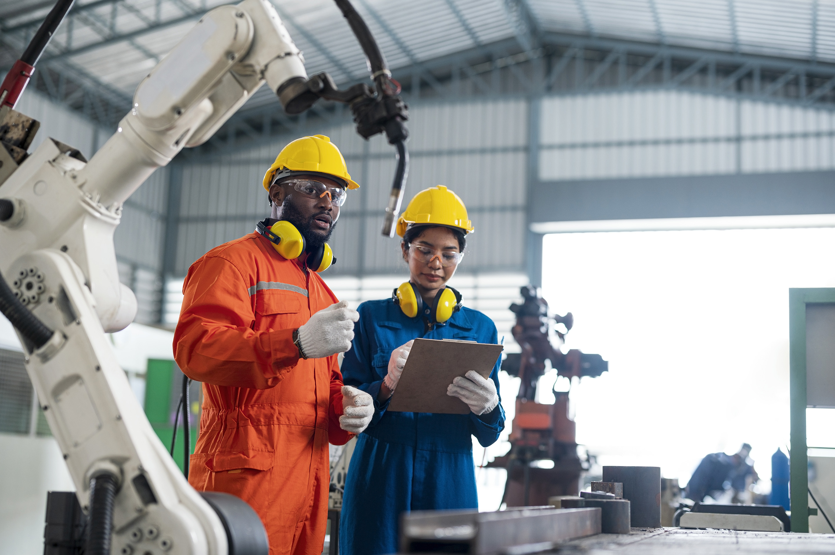 Two workers in a high-tech factory or warehouse standing next to a robotic arm.