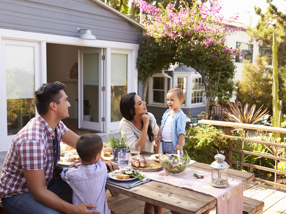 Family of four sitting at a picnic table on a sunny wood backyard deck.