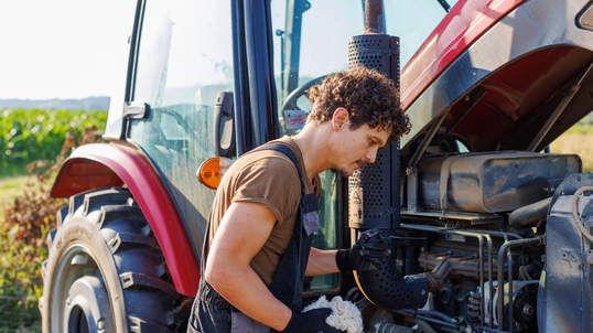 A farmer performs maintenance on his tractor on a farm.