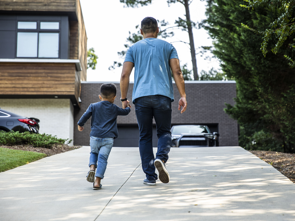 Father holding the hand of his young son while walking up a driveway.