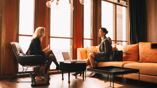 female lawyers discussing while sitting by window at office