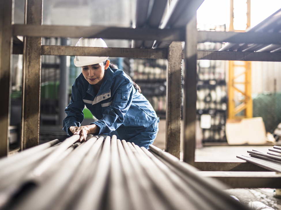Worker in hard hat pulling a metal rod off a shelf in a high-risk product manufacturing plant.