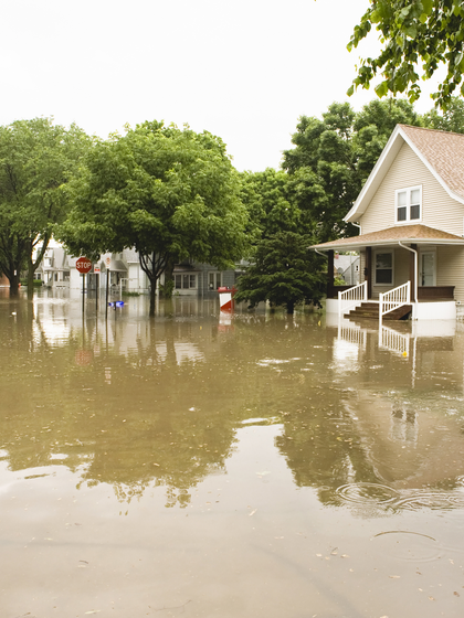 A house sits with water up to its porch in the stillness of a flooded neighborhood street. 