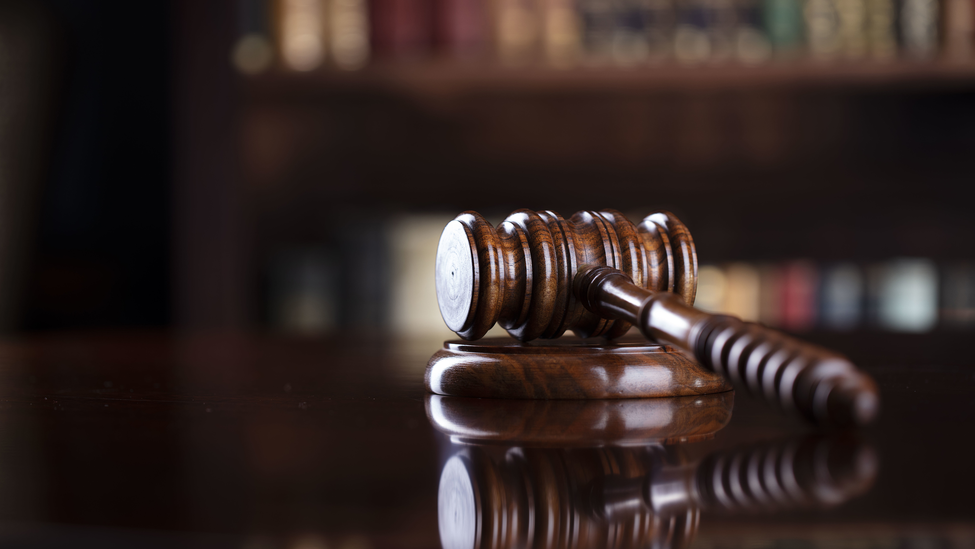 Judge's gavel on brown shining table and bookshelf background