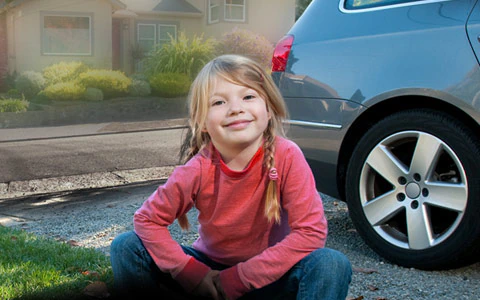 Girl sitting in front of car.