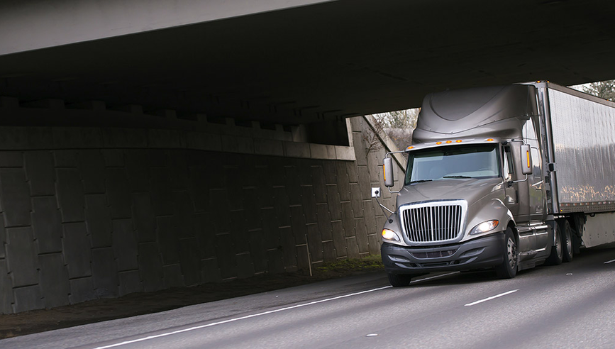 Grey truck driving under a bridge 