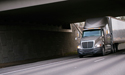 Grey truck driving underneath bridge