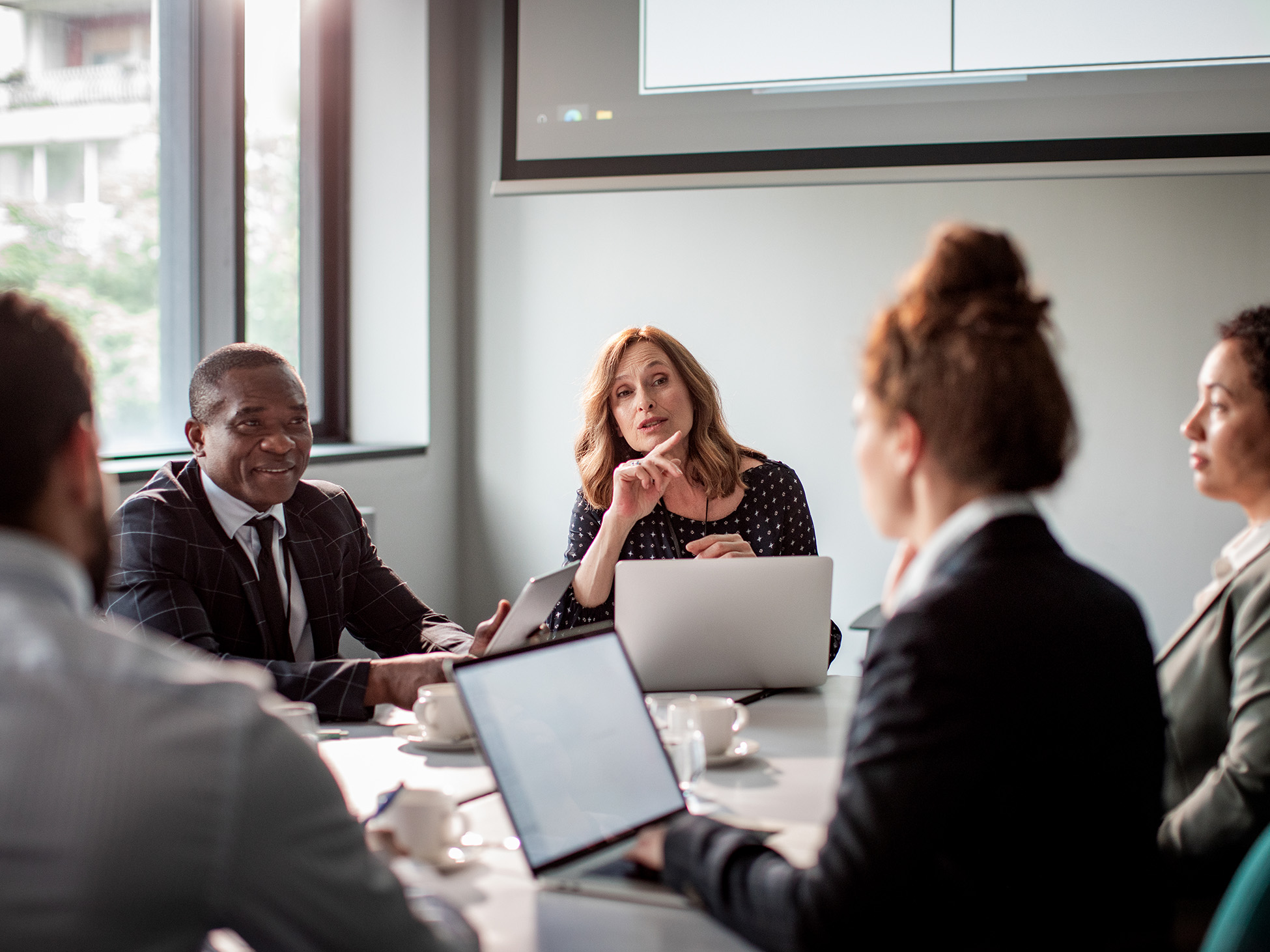 Group of female and male agents sitting with laptops during a meeting in a conference room.