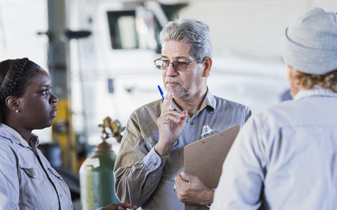 Three team members having a meeting while standing in a mechanics garage. 